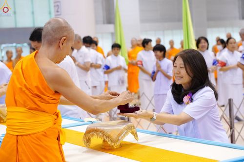 พระภิกษุกำลังส่งมอบพระของขวัญให้แก่หญิงสาวในชุดสีขาวท่ามกลางผู้เข้าร่วมพิธี