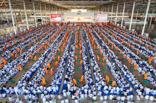 พุทธศาสนิกชนชุดขาวจำนวนมากนั่งเรียงแถวตักบาตรพระภิกษุสงฆ์ภายในอาคารสภาธรรมกายสากล