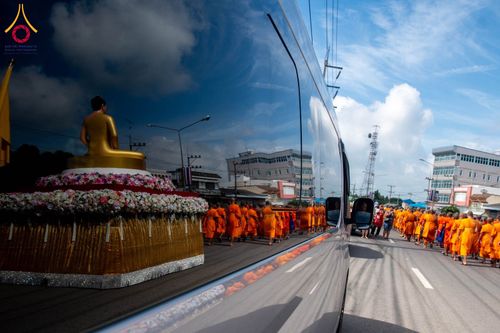 ภาพสะท้อนบนตัวรถตู้เห็นขบวนพระภิกษุสงฆ์และพระพุทธรูปบนรถแห่บนถนน