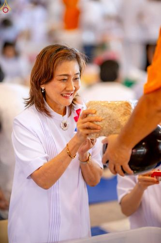หญิงสาวสวมชุดสีขาวกำลังตักบาตรด้วยถุงข้าวสารในพิธีทางศาสนา