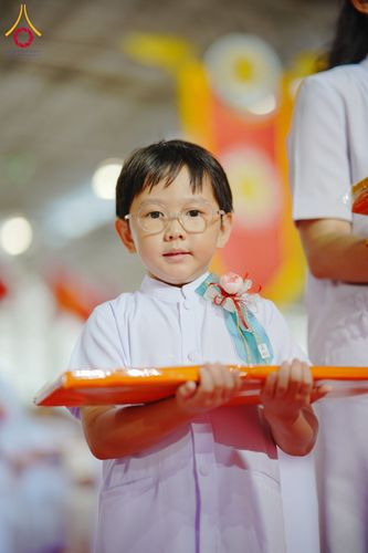 เด็กชายสวมแว่นตาและชุดสีขาวถือพานสีส้มในงานพิธี
