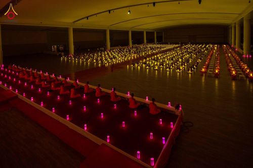 กลุ่มคนนั่งปฏิบัติธรรมในห้องโถงกว้างท่ามกลางแสงเทียนที่วางเรียงรายเป็นระเบียบ