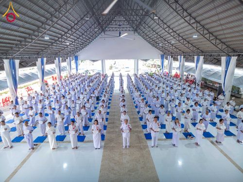 กลุ่มผู้เข้าร่วมโครงการอบรมอุบาสกแก้วและอุบาสิกาแก้วสวมชุดสีขาว ยืนเรียงแถวอย่างเป็นระเบียบภายในอาคารปฏิบัติธรรม