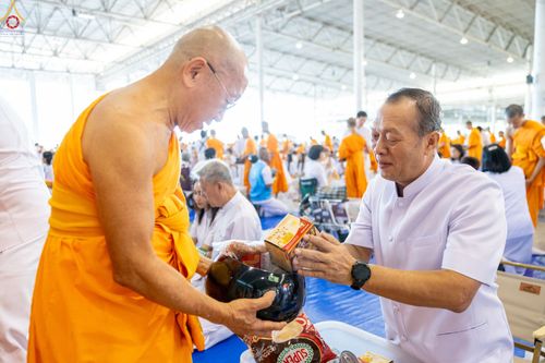 ชายสวมชุดสีขาวกำลังใส่สิ่งของลงในบาตรของพระภิกษุสงฆ์ในพิธีตักบาตร