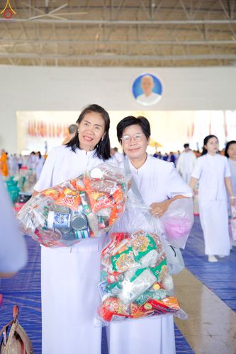 หญิงสองคนสวมชุดสีขาวถือถุงใส่ของแห้งเพื่อเตรียมตักบาตรในงานบุญ