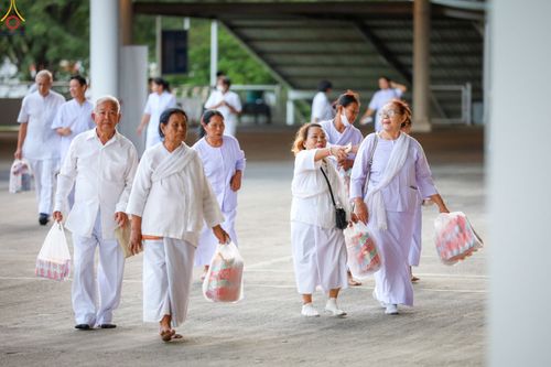 กลุ่มคนสวมชุดสีขาวถือถุงอาหารแห้งเดินในพื้นที่วัด