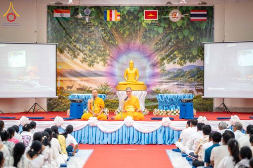 พระสงฆ์สองรูปกำลังแสดงธรรมบนเวทีต่อหน้าพุทธศาสนิกชนจำนวนมากในห้องประชุม