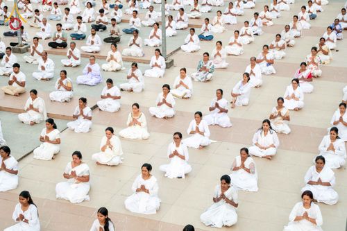 กลุ่มผู้ปฏิบัติธรรมสวมชุดสีขาวนั่งพนมมือเรียงแถวบนพื้นปูหินในพื้นที่โล่ง