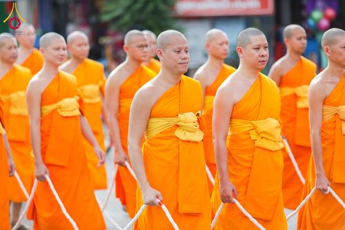 พระภิกษุสงฆ์หลายรูปสวมจีวรสีส้มเดินแถวถือสายสิญจน์ในพิธีทางศาสนา