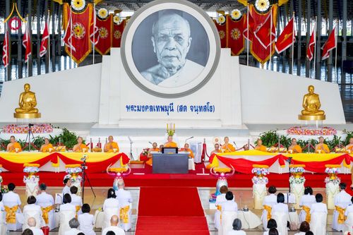 พระภิกษุสงฆ์และสาธุชนร่วมพิธีทางศาสนาภายในอาคารขนาดใหญ่ที่มีภาพพระมงคลเทพมุนีเป็นฉากหลัง