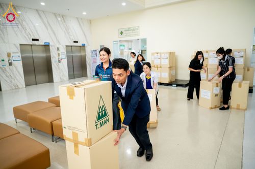 กลุ่มคนกำลังช่วยกันขนย้ายกล่องกระดาษบรรจุยาภายในโถงอาคารศูนย์การแพทย์