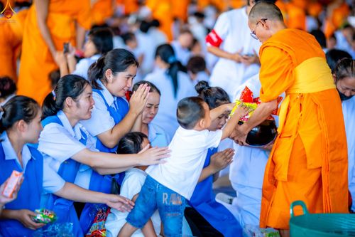 เด็กชายกำลังใส่บาตรพระภิกษุสงฆ์ท่ามกลางพุทธศาสนิกชนที่มาร่วมทำบุญตักบาตร