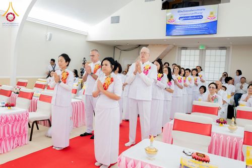กลุ่มคนสวมชุดสีขาวกำลังยืนพนมมือร่วมพิธีทางศาสนาภายในอาคาร