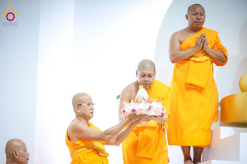 พระภิกษุสงฆ์ในจีวรสีเหลืองทองกำลังประกอบพิธีทางศาสนาและถือพานดอกไม้ที่มีเกศดอกบัวตูมบรรจุพระบรมสารีริกธาตุ