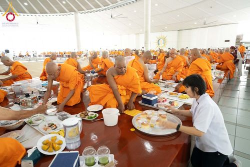 พระภิกษุสงฆ์กำลังฉันภัตตาหารภายในหอฉันขนาดใหญ่ โดยมีเจ้าหน้าที่คอยให้บริการจัดเตรียมอาหาร