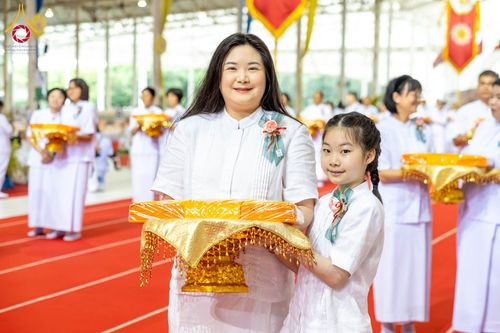 หญิงและเด็กหญิงถือพานพุ่มผ้าไตรสีทองในพิธีทางศาสนา