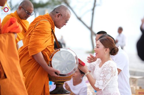 หญิงสาวกำลังประเคนของใส่บาตรแด่พระสงฆ์ในพิธีตักบาตรริมชายหาด