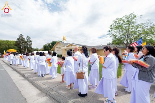 กลุ่มคนสวมชุดสีขาวถือผ้าไตรเดินเป็นแถวหน้าอาคารวัดพระธรรมกายซิลิคอนวัลเลย์