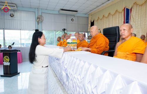 หญิงสวมชุดสีขาวกำลังประเคนพานพุ่มบรรจุพระบรมสารีริกธาตุแด่พระภิกษุสงฆ์ภายในอาคาร