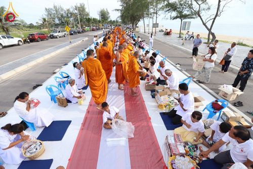พระสงฆ์เดินรับบิณฑบาตจากพุทธศาสนิกชนที่นั่งเรียงรายบนพื้นถนนเลียบชายหาด