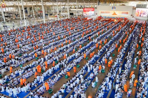 พุทธศาสนิกชนจำนวนมากในชุดขาวและพระภิกษุสงฆ์กำลังร่วมพิธีตักบาตรภายในอาคารขนาดใหญ่