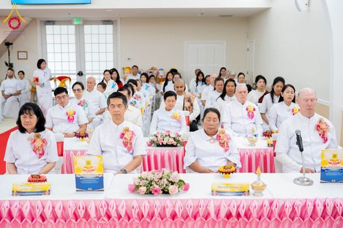 กลุ่มคนสวมชุดสีขาวนั่งพนมมือหรือหลับตาทำสมาธิในพิธีทางศาสนาภายในอาคาร