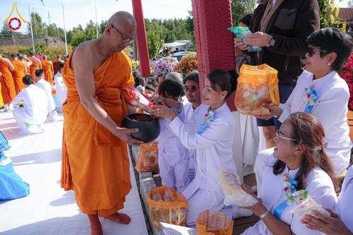 พระภิกษุสงฆ์รับบิณฑบาตจากกลุ่มพุทธศาสนิกชนที่สวมชุดสีขาวในพิธีทำบุญ