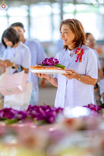หญิงไทยสวมชุดสีขาวถือถาดอาหารแห้งและดอกไม้ในพิธีตักบาตร