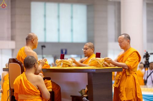 พระภิกษุสงฆ์ในจีวรสีเหลืองกำลังประกอบพิธีมอบพระของขวัญบนโต๊ะพิธีภายในอาคาร