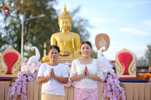หญิงสองคนยืนพนมมือหน้าพระพุทธรูปสีทองในพิธีทำบุญตักบาตร