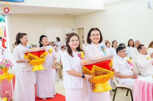 กลุ่มสาธุชนสวมชุดขาวถือพานพุ่มผ้าป่าเดินเข้าสู่พื้นที่ประกอบพิธีภายในอาคาร