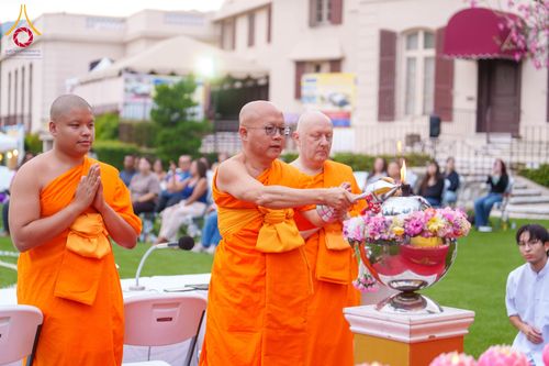 พระภิกษุสงฆ์กำลังจุดประทีปในพานพุ่มดอกไม้ในกิจกรรมนั่งสมาธิกลางแจ้ง