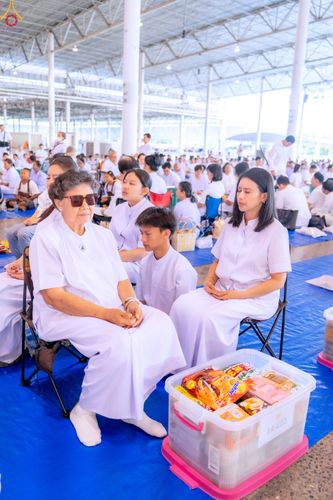กลุ่มคนสวมชุดขาวนั่งพนมมือเตรียมตักบาตรภายในอาคารขนาดใหญ่