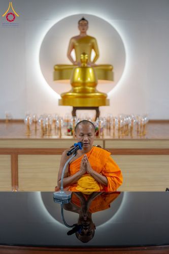 พระภิกษุประนมมือสวดมนต์หน้าไมโครโฟน โดยมีพระพุทธรูปเป็นฉากหลัง