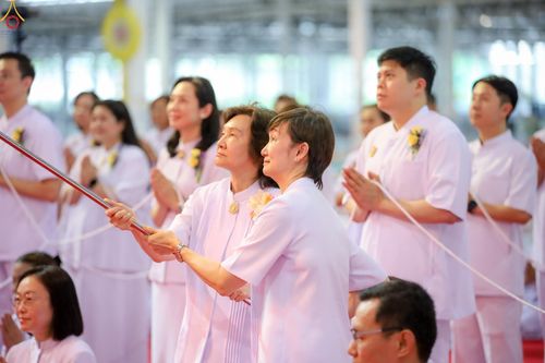 กลุ่มคนสวมชุดสีขาวกำลังร่วมพิธีจุดเทียนใจ โดยมีผู้หญิงสองคนถือคบเพลิงอยู่ด้านหน้า