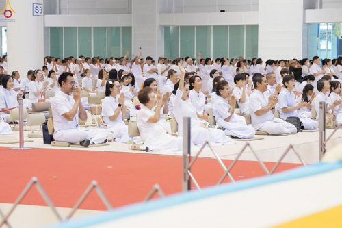 กลุ่มคนสวมชุดสีขาวนั่งพนมมือปฏิบัติธรรมภายในห้องโถงขนาดใหญ่