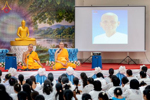 พระภิกษุสองรูปในชุดจีวรสีเหลืองนั่งบนเวทีเพื่อบรรยายธรรมต่อหน้าผู้เข้าร่วมโครงการจำนวนมาก