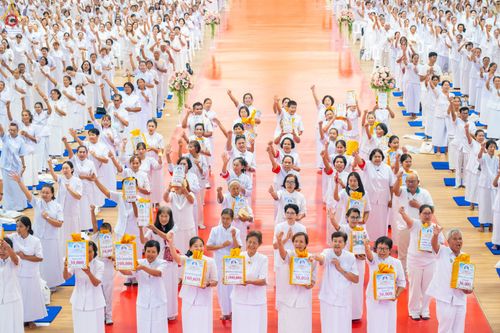 พุทธศาสนิกชนชุดขาวจำนวนมากถือป้ายทำบุญกฐินร่วมกิจกรรมสัมมนาภายในอาคาร