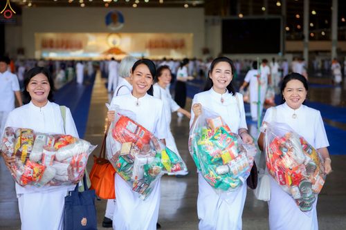 หญิงไทยสี่คนสวมชุดสีขาวถือถุงใส่ข้าวสารอาหารแห้งเพื่อเตรียมตักบาตรภายในอาคาร