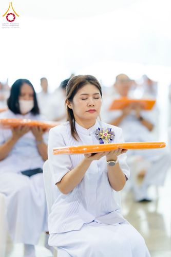 หญิงสาวสวมชุดขาวนั่งประคองผ้าไตรจีวรสีเหลืองในพิธีทางศาสนา