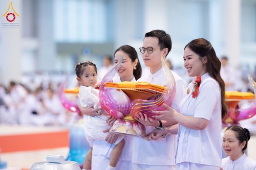 กลุ่มคนในชุดสีขาวถือพานพุ่มดอกบัวประดับผ้าไตรในพิธีทางศาสนา
