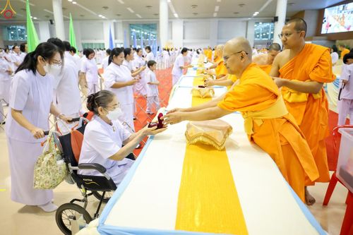 พระภิกษุสงฆ์มอบพระของขวัญให้แก่หญิงสูงวัยบนรถเข็นในพิธีทางศาสนา