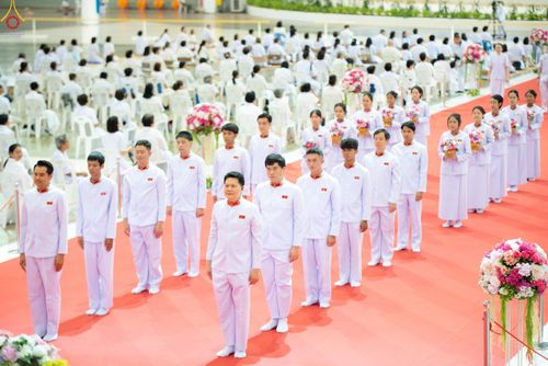 กลุ่มคนในชุดสีขาวเข้าแถวเรียงรายบนพรมสีแดงภายในอาคารเพื่อร่วมพิธีทางศาสนา