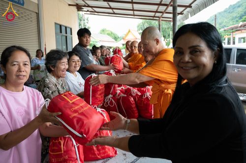 พระสงฆ์ในจีวรสีส้มและเจ้าหน้าที่กำลังส่งมอบถุงยังชีพสีแดงให้กับประชาชนด้วยรอยยิ้ม