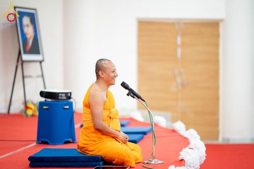 พระภิกษุสงฆ์นั่งพูดผ่านไมโครโฟนบนอาสนะในห้องโถง