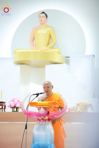 พระภิกษุสงฆ์กำลังกล่าวธรรมะหน้าแท่นบรรยาย โดยมีพระพุทธรูปสีทองประดิษฐานอยู่ด้านหลัง