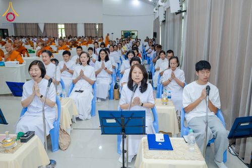 กลุ่มคนสวมชุดขาวนั่งพนมมือฟังการบรรยายในห้องสัมมนาที่มีพระภิกษุสงฆ์ร่วมงาน