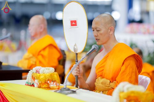 พระภิกษุถือพัดยศและพูดผ่านไมโครโฟนในงานพิธีทางศาสนา