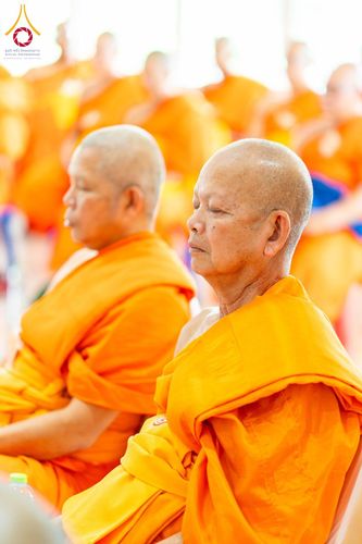 พระภิกษุสงฆ์หลายรูปห่มจีวรสีส้มกำลังนั่งหลับตาทำสมาธิในพิธีทางศาสนา