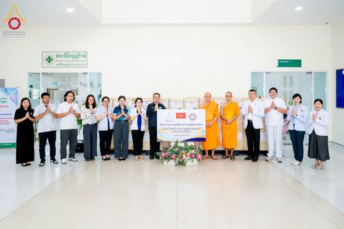 กลุ่มบุคคลและพระภิกษุยืนเรียงแถวหน้าป้ายโครงการบริจาคยาและเวชภัณฑ์ภายในอาคาร